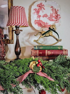 Christmas still life with gingham lamp, vintage plate, books, and pine garland with red and gold ornaments