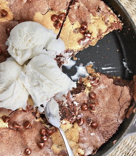 Vanilla ice cream scoops on top of a chocolate chip skillet cookie with spoon