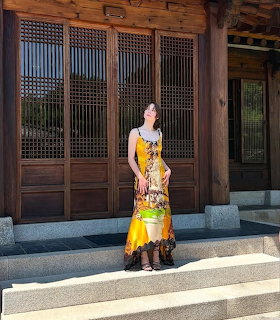 Woman in yellow floral dress posing outdoors before traditional wooden building
