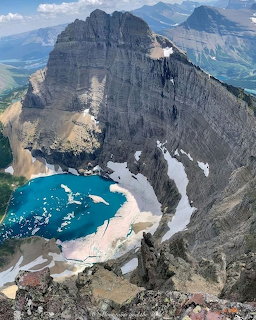 Turquoise alpine lake in a rocky mountain cirque with steep cliffs and snow patches