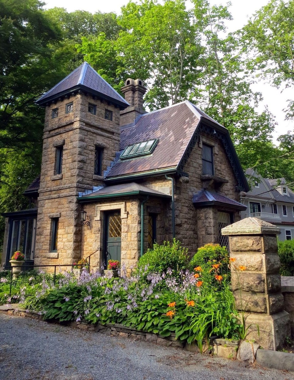 Stone cottage house with a tower, garden flowers, and trees