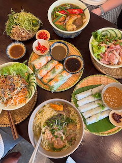 Overhead view of various Vietnamese dishes including pho, fresh spring rolls, noodles, and vegetables on a wooden table