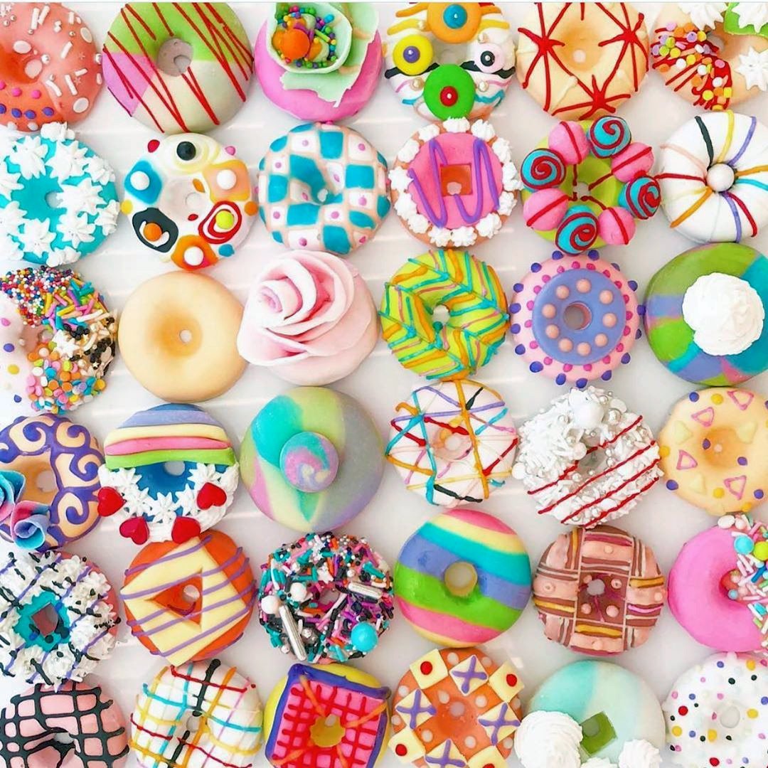 Assortment of colorfully decorated doughnuts with various toppings and patterns viewed from above