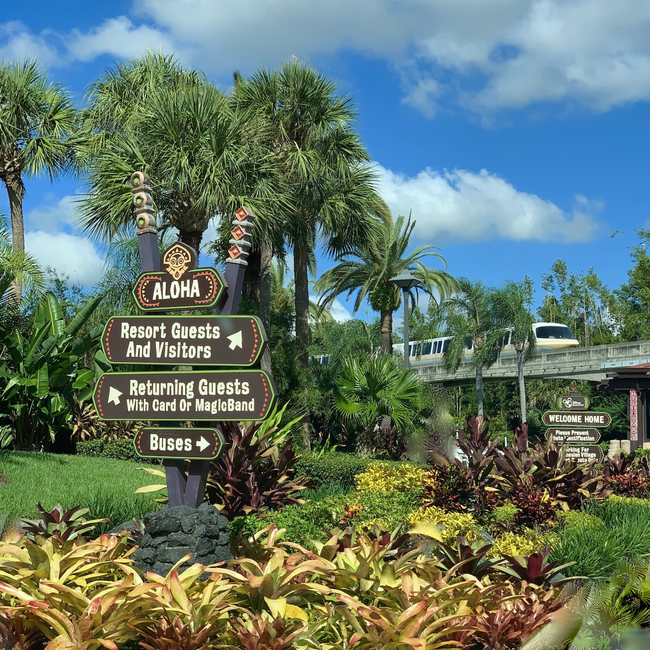 Wooden resort sign with tropical landscaping and palm trees at Disney Polynesian Hotel entrance
