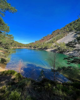 Blue mountain lake bordered by trees and hills beneath a clear sky