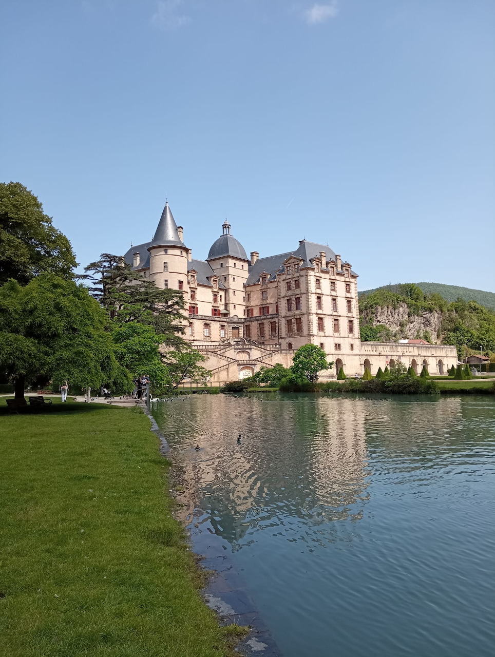 Grand French château with round towers beside peaceful lake with reflection