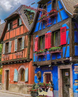 Traditional half-timbered houses in bright blue and coral colors with flower boxes on a street in Alsace, France