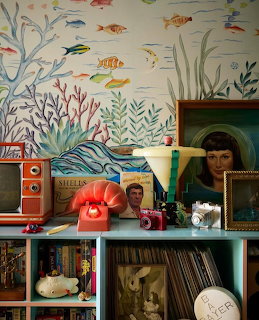 Teal bookshelf with vintage cameras, red rotary phone, paintings, and retro TV against underwater mural wallpaper