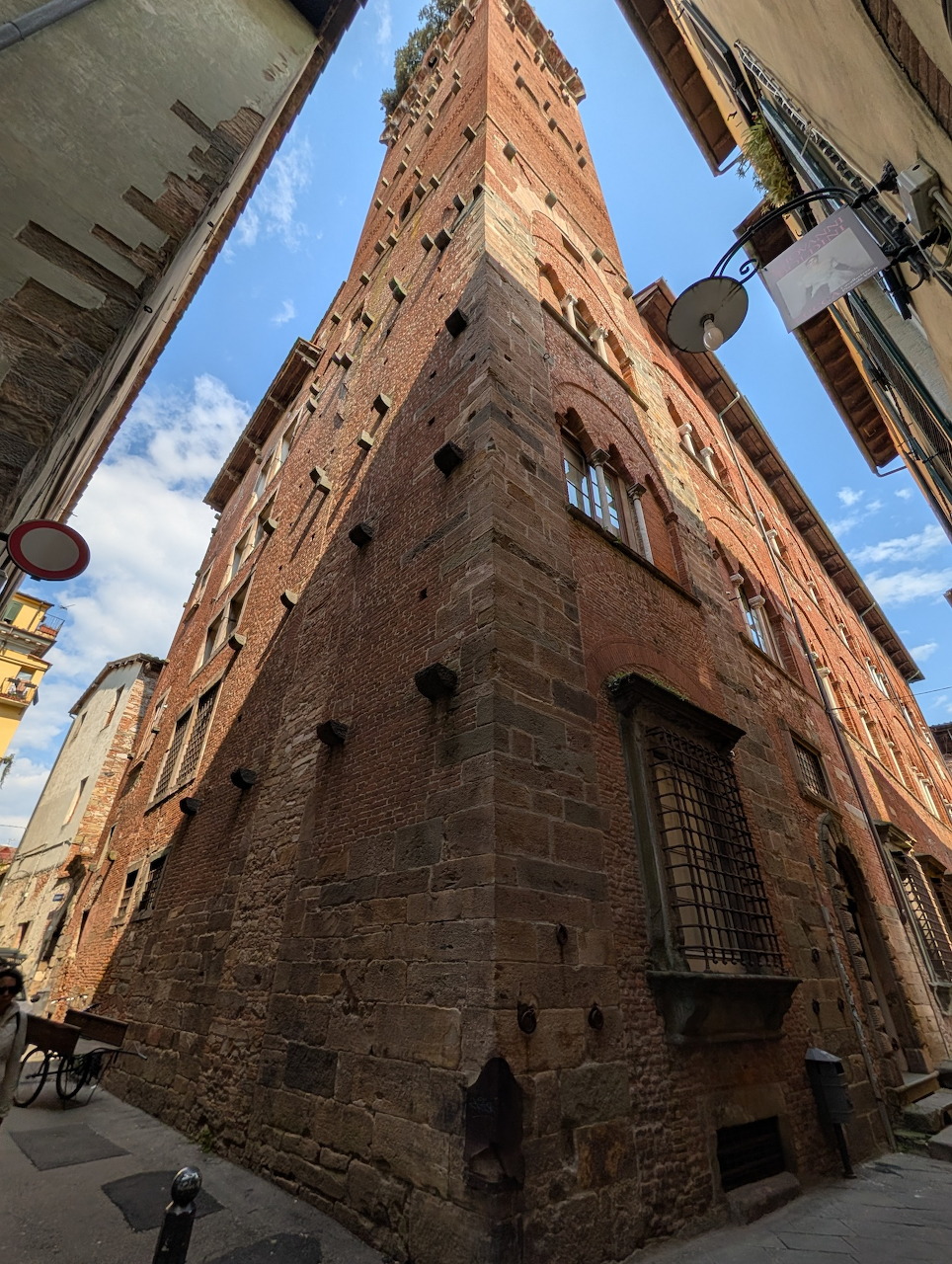 Tall medieval brick tower viewed from street level in Lucca, Italy