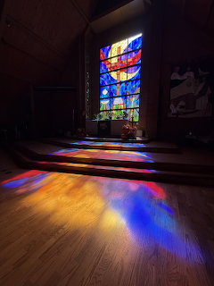 Stained glass window casting colorful light patterns on a wooden church floor