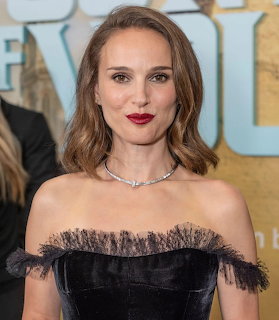 Woman in an off-shoulder black dress with red lipstick posing in front of an event backdrop.