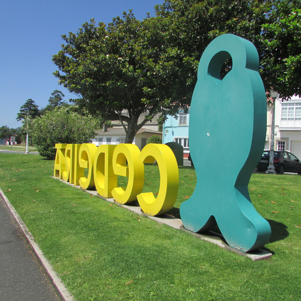 Yellow letter sculpture and teal abstract shape on a grassy lawn near a street