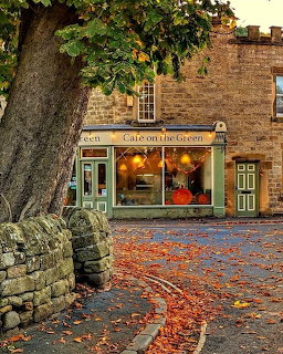Stone building coffee shop with green trim and warm lights, autumn leaves scattered on cobblestone ground