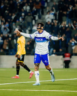 Soccer player in white and blue jersey celebrating with arms spread wide on field during night match