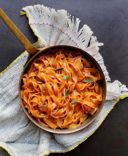 Copper pan with orange ribbon pasta garnished with sage leaves on a white fringed napkin