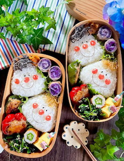 Two bento boxes with snowman rice balls decorated with vegetables, fried items, strawberries, and garnishes