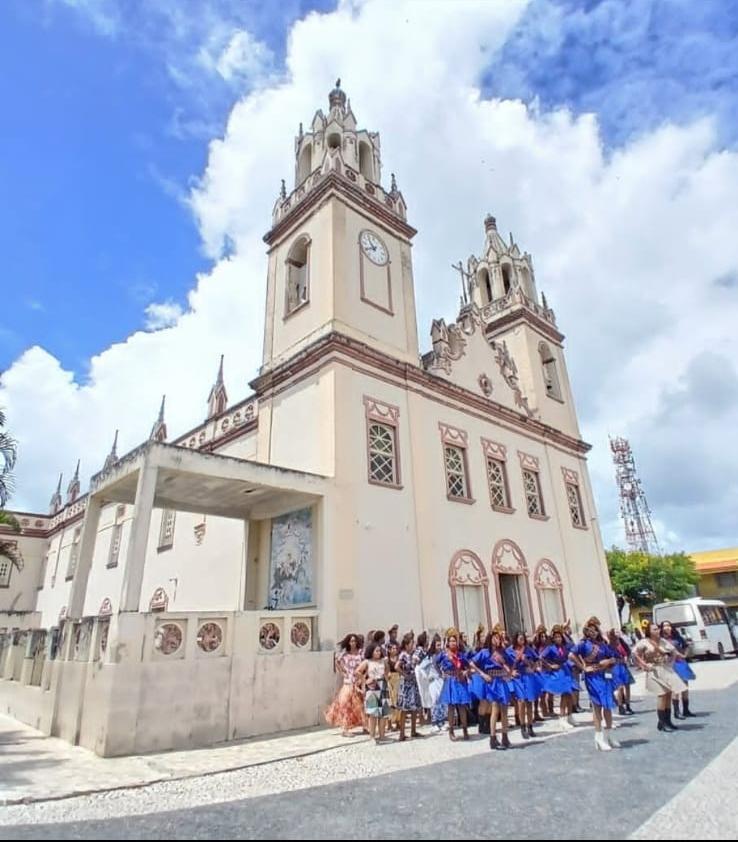 White colonial church with twin towers and a procession of people in blue uniforms in front under a blue sky