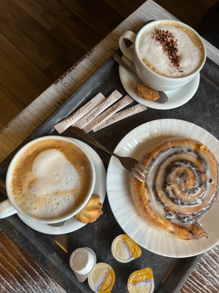 Cappuccino with latte art and cocoa powder next to a cinnamon roll