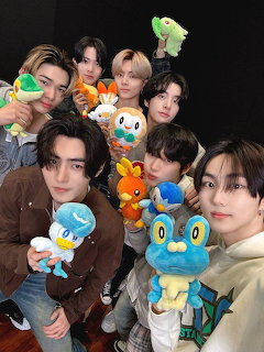 Six young men posing with colorful Pokemon plush toys against a dark background
