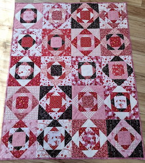 Pink and red patchwork quilt with geometric blocks and floral patterns on wooden floor