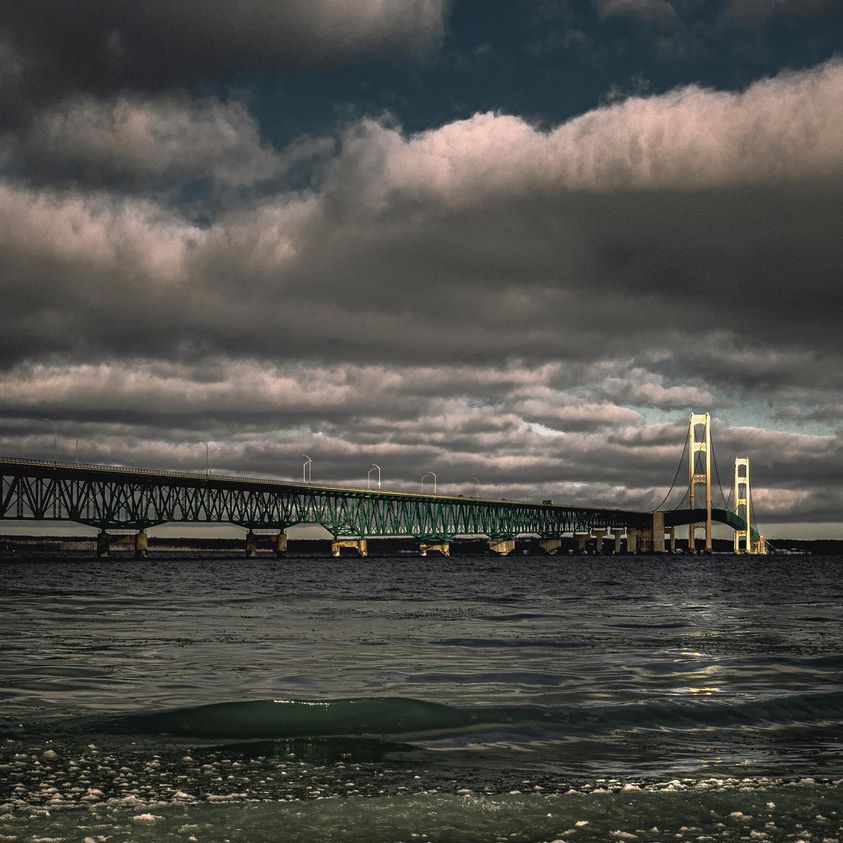Mackinac Bridge under dramatic storm clouds with dark water in foreground