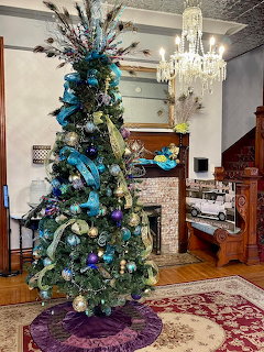 Decorated Christmas tree with blue ribbon in elegant mansion room with chandelier and fireplace