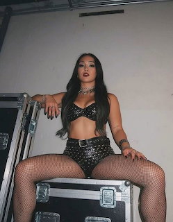 Woman with long dark hair in studed black outfit sitting on a road case backstage