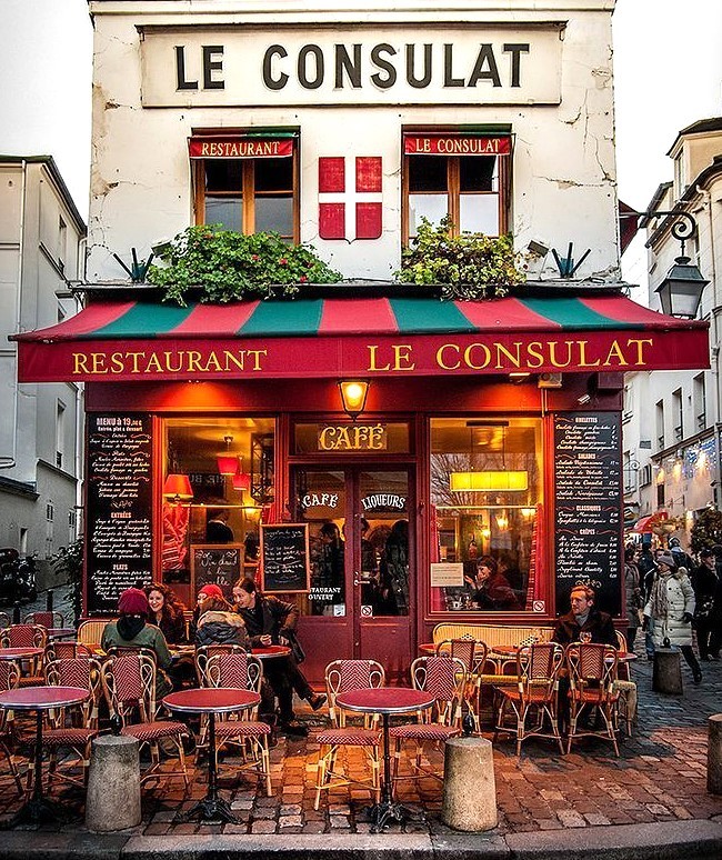 Le Consulat restaurant facade at night in Montmartre, Paris with red awning and glowing interior