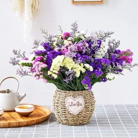 Purple and white flower bouquet in a woven basket with a teapot nearby