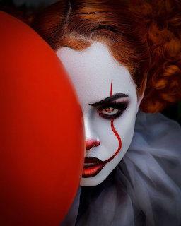 Clown with white face paint, red tear marking, orange hair, and red balloon in dramatic lighting