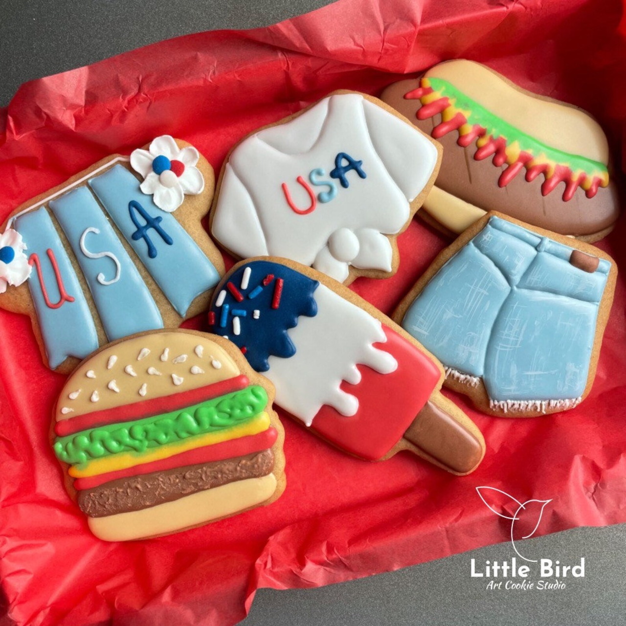 Assorted decorated cookies with American summer themes including hamburger, hot dog, popsicle, and USA flag designs