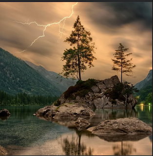 Lightning strikes over a mountain lake with pine trees on a rocky island during a storm