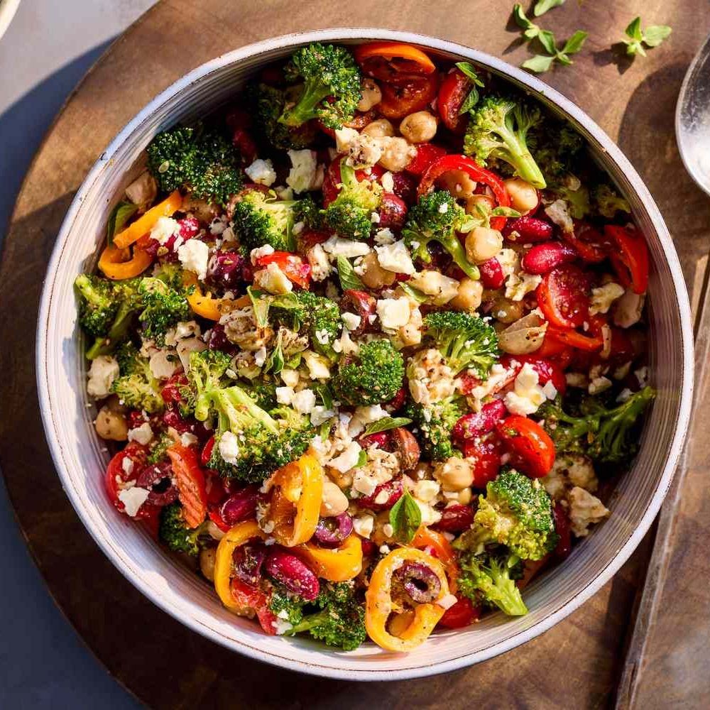 Bowl of roasted vegetables with broccoli, peppers, cauliflower, chickpeas, and herbs on wooden table