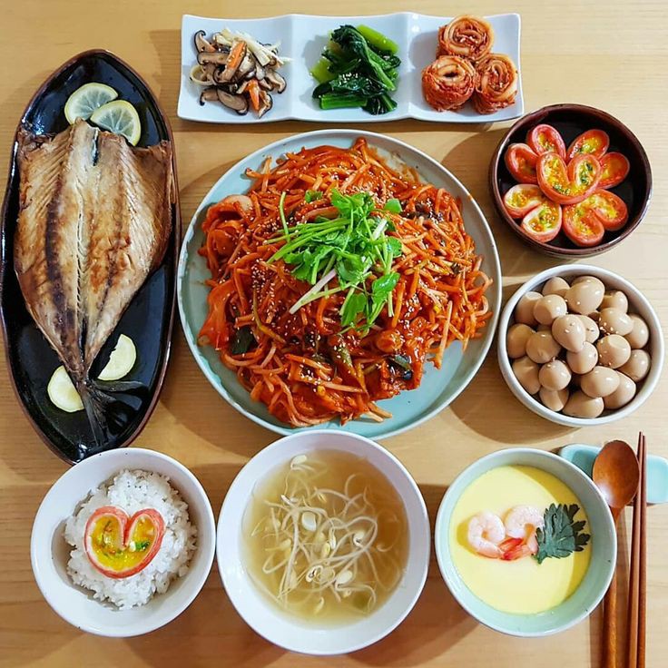 Overhead view of Korean dishes including spicy noodles, grilled fish, soup, and side dishes on a table