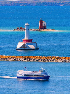 White lighthouse on a small island with a ferry boat crossing blue water