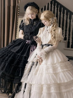 Two women in black and white Gothic Lolita dresses with lace and ruffles posing on a staircase