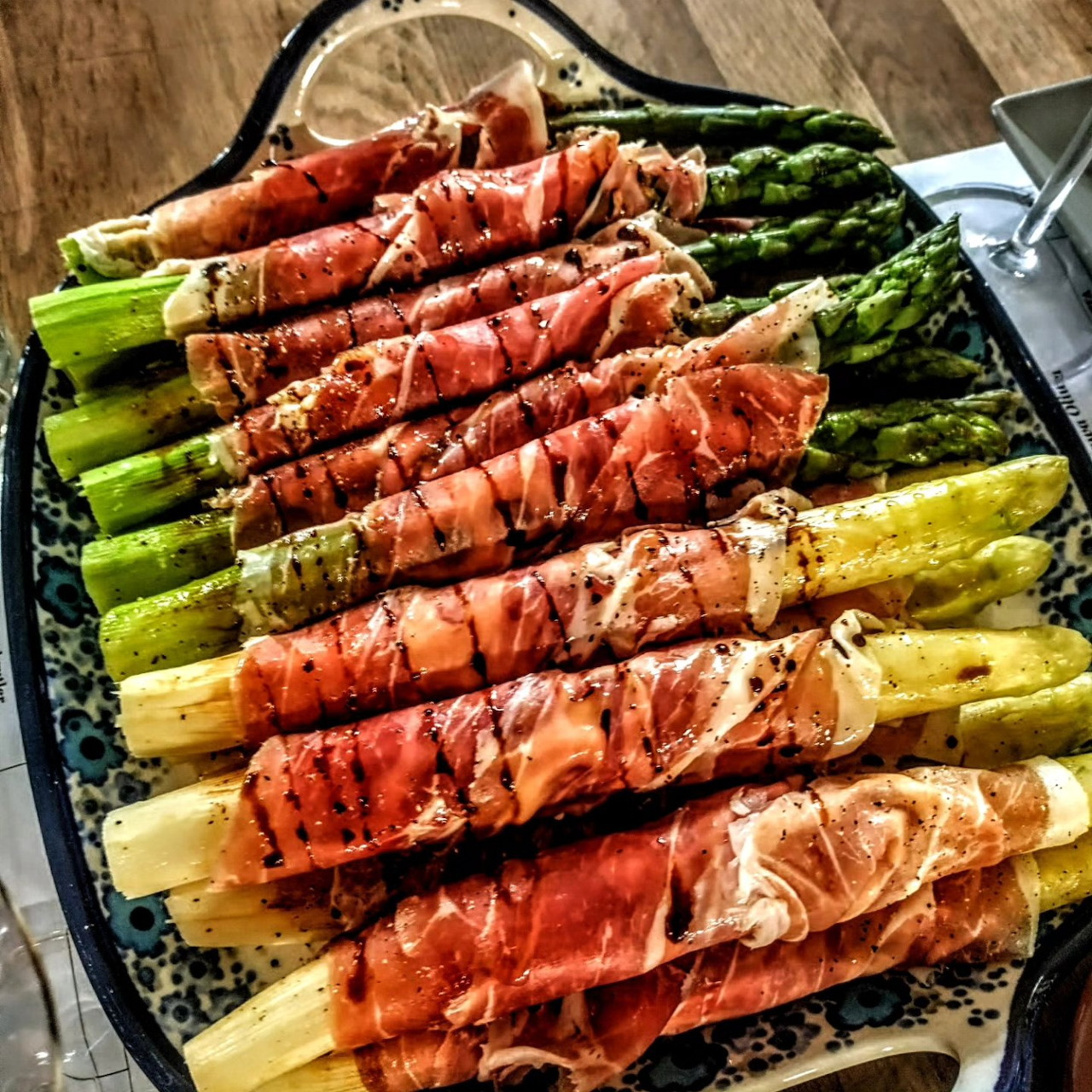 White and green asparagus wrapped in prosciutto on a patterned platter