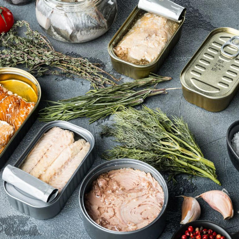 Assorted canned fish with herbs and garlic arranged on a dark surface