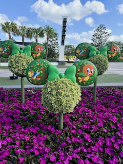 Disney character topiary display above purple flowers at Epcot on a sunny day