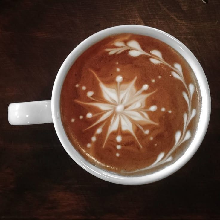 Overhead view of a white cup of coffee with flower latte art on a dark wood surface