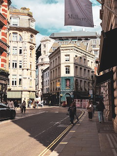 London street scene with historic buildings, pedestrians, and a Mulberry store flag