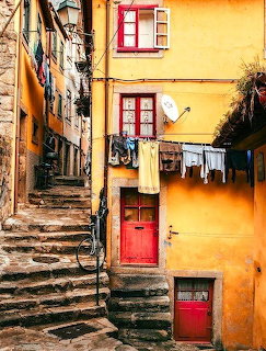 Narrow stone stairs in a rustic Porto alley with yellow buildings, red doors, and hanging laundry