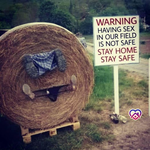 Round hay bale next to white warning sign in grassy field