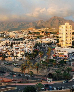 Aerial view of Las Américas coastal town in Tenerife with buildings, palm trees, and mountains at sunset