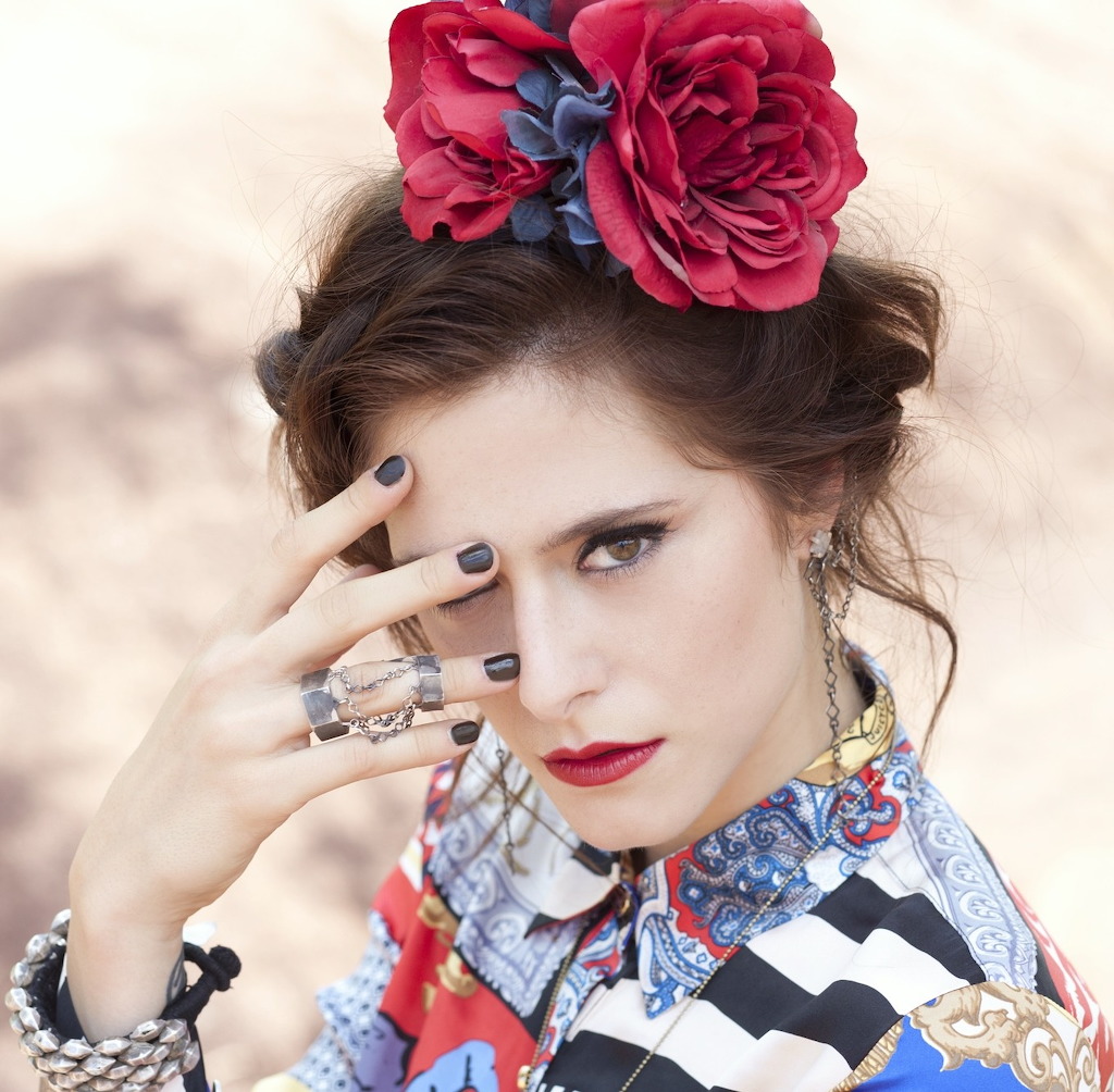 Woman with red flower crown, dark nails, red lipstick, and patterned colorful top