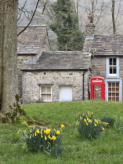 Stone cottage with a red telephone booth and yellow daffodils in a grassy garden