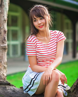 Young woman sitting on a tree trunk outdoors in a striped shirt and white shorts
