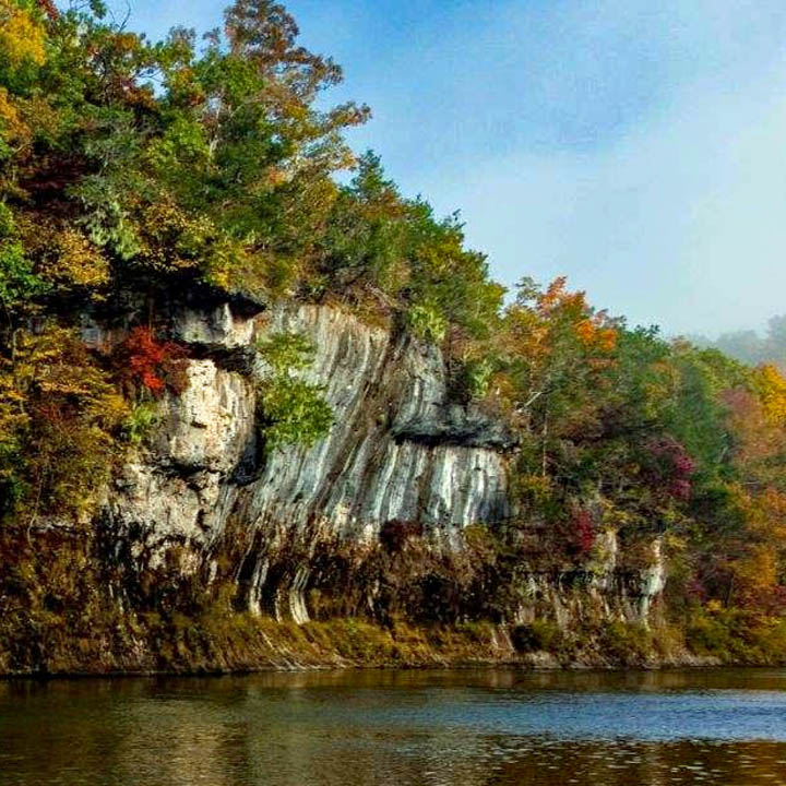 Tall rocky cliffs with trees reflecting in calm lake water on sunny day