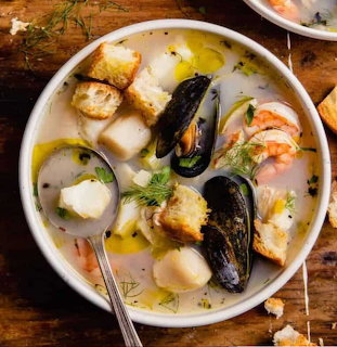 Bowl of seafood soup with mussels, shrimp, scallops, bread chunks, and dill in creamy broth