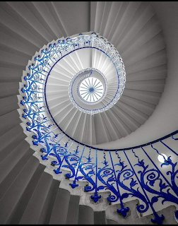 Spiral staircase with blue ornate railing viewed from below leading to circular skylight